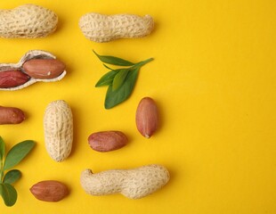 Fresh peanuts and leaves on yellow table, flat lay. Space for text
