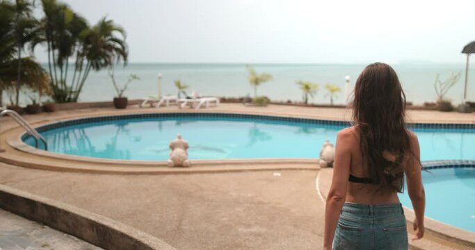 A woman standing in front of a clear blue swimming pool at a resort on Thailands Koh Phangan Island.