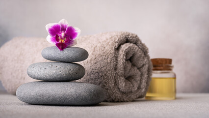 Fototapeta na wymiar Spa still life with smooth pebbles, a rolled gray towel, and a vibrant purple orchid