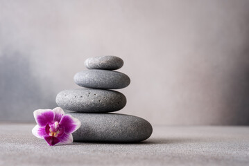 Obraz na płótnie Canvas Zen stones and pink orchid flower on gray background as spa concept