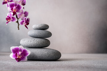 Obraz na płótnie Canvas Zen stones and pink orchid flower on gray background as spa concept