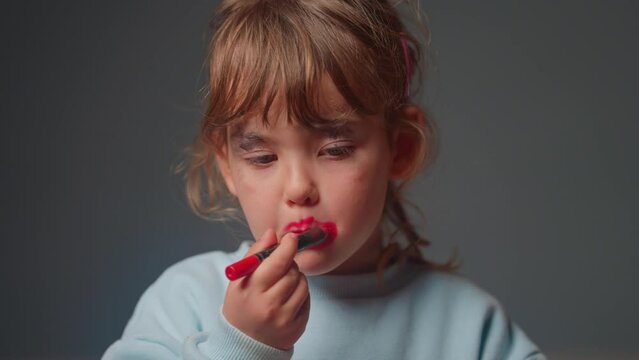 Cute little girl trying on lipstick for the first time. Happiness, fun, entertainment