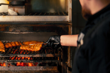 close-up of a professional kitchen a chef in a black jacket near a hot grill oven turns over ribs