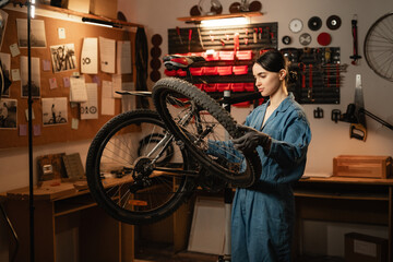 Cute Caucasian woman holding and repairing bicycle wheel in bicycle workshop.