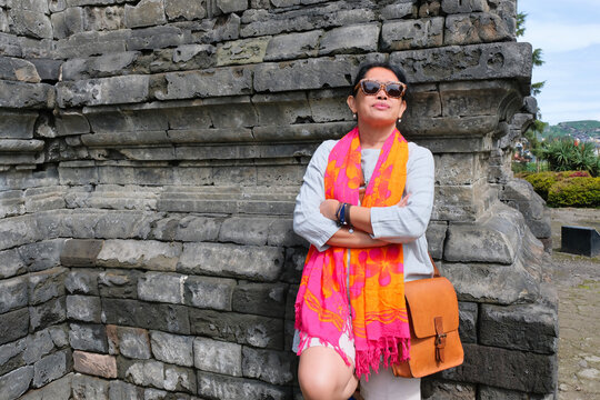 A woman wearing a bright shawl and sunglasses leaned against a temple