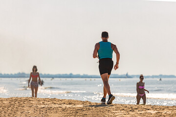 A man jogging along the seashore on a sandy beach on a summer day during a heatwave; a fit man running along a sandy beach wearing sports clothes