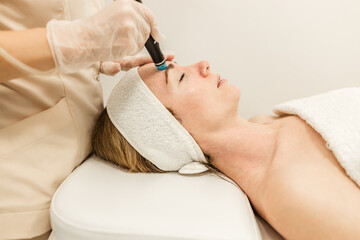 Beautician in gloves conducts vacuum cleaning and polishing face skin  in cosmetology clinic. Professional moisturizing and rejuvenating hardware procedures for modern people.