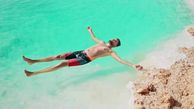 young man floating in bright blue salt pool wearing bathing suit in Siwa Oasis, Egypt