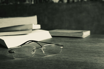 Classic glasses and pile of books on the table, monochrome. Literature concept. Eyeglasses next to old books. Education and knowledge. Research concept. Book club concept. Read and study.  - 783183143