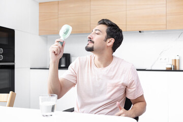 Tired and overheated man suffering from a heat attack uses an electric handy fan to cool himself...