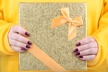 Close-up of a gift box in female hands with a stylish blackberry-colored manicure.