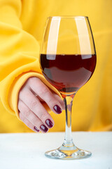 A woman's hand with a fashionable blackberry-colored manicure takes a glass of wine.