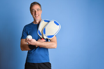 Smiling man in sportswear with pickleball  equipment blue isolated background