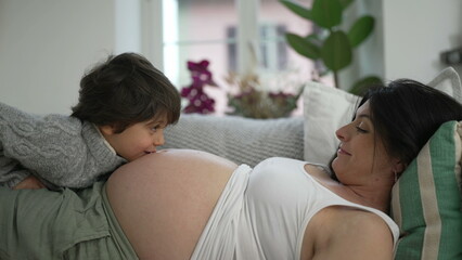 Beautiful maternal scene of pregnant mother bonding with son. 5 year old boy interacting with mom's...