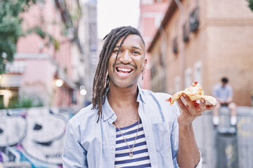 portrait of an enthusiastic young man on the street with a slice of pizza in his hand
