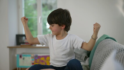 Cute 5 year old little boy flexing arms showing his strength at home, Proud Display of His Growing...
