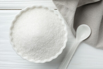 Granulated sugar in bowl and spoon on white wooden table, top view