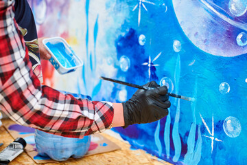 Female artist hand applies small brushstrokes of paint with paintbrush to canvas creating picture...