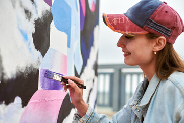Female painter draws picture with paintbrush on canvas for outdoor street exhibition, close up side...