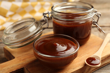Tasty barbeque sauce in bowl, jar and spoon on wooden table, closeup