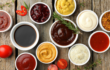 Different tasty sauces in bowls and ingredients on wooden table, flat lay