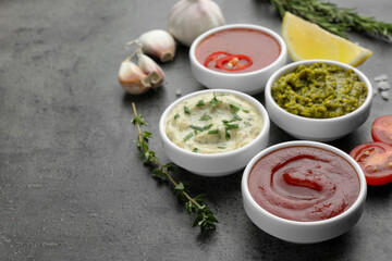 Different tasty sauces in bowls and ingredients on grey table, space for text
