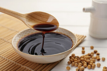 Taking tasty soy sauce from bowl with spoon on white wooden table, closeup