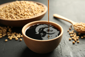 Pouring tasty soy sauce into bowl on black table, closeup
