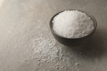 Natural salt in bowl on grey table, space for text