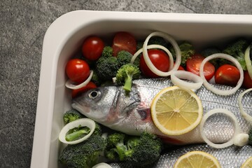 Raw fish with vegetables and lemon in baking dish on grey table. top view