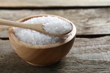 Organic salt in bowl and spoon on wooden table, closeup. Space for text
