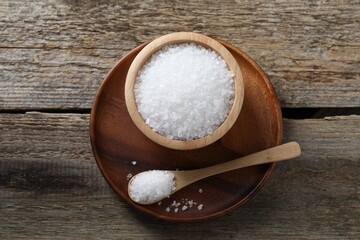 Organic salt in bowl and spoon on wooden table, top view