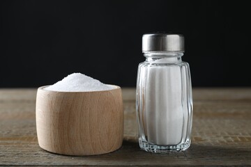 Organic salt in bowl and glass shaker on wooden table, closeup
