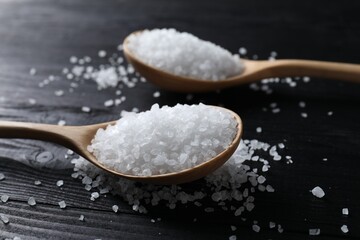 Fototapeta na wymiar Organic salt in spoons on black wooden table, closeup