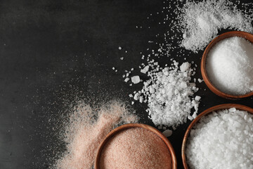 Different types of organic salt in bowls on black table, flat lay. Space for text
