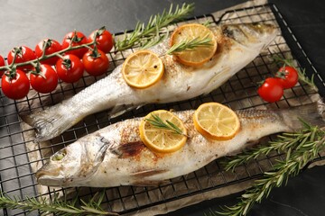 Baked fish with tomatoes, rosemary and lemon on black textured table, closeup