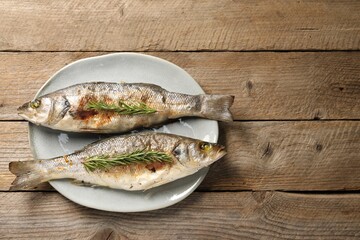 Delicious baked fish and rosemary on wooden table, top view. Space for text