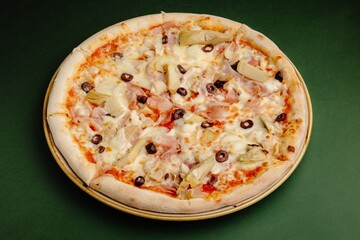 Delicious pizza with ham, cheese, olives, and artichokes on green background