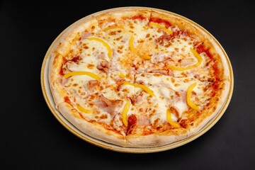 Top view of a pizza with ham and bell peppers on a black background