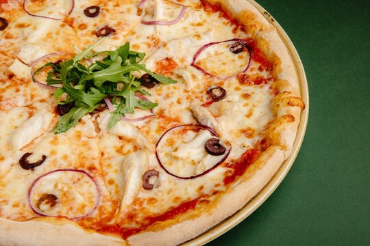 Delicious pizza with olives, red onion, and arugula on a green background