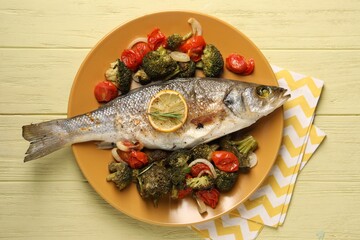 Delicious baked fish and vegetables on yellow wooden table, top view