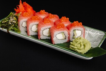 Scrumptious sushi rolls with caviar topping and wasabi paste on a green leaf plate with chopsticks.