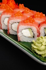 Sushi rolls with salmon, cream cheese, and caviar on the plate with wasabi and ginger