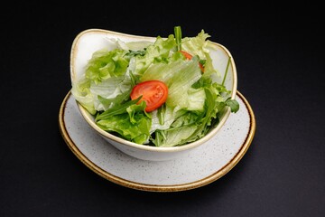 Fresh organic mixed greens salad with tomatoes and parsley in a white bowl isolated on black.
