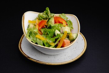 Vegetable Salad with Lettuce, Cucumber, Tomato, and Bell Pepper on Black Background.