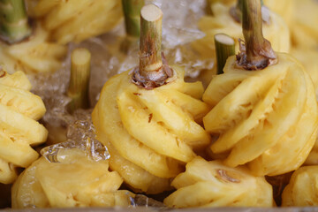 Close up to peeled yellow pineapple fruit kept fresh and cool with ice cubes and sold as a healthy vegan summer snack, evoking a sense of joy and wellness