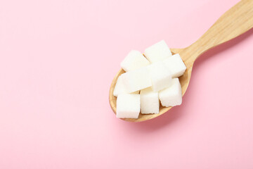 White sugar cubes in wooden spoon on pink background, top view. Space for text