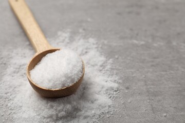 Natural salt and wooden spoon on grey table, closeup. Space for text
