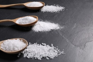 Natural salt and wooden spoons on black table, closeup. Space for text