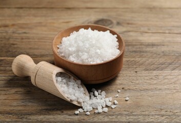 Natural salt with bowl and scoop on wooden table, closeup